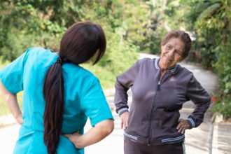 A nurse guides an elderly woman in hip stretching exercises to improve mobility and health.