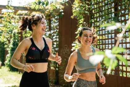 Two happy friends running on a sunny day on wooden walkway with green leaves,leading a healthy life.